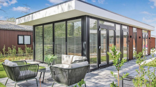 Lodge Forest villa moderne avec grandes baies vitrées, coin salon extérieur et jardin verdoyant sous ciel bleu.