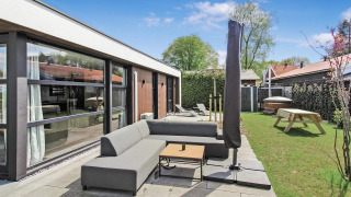 Zona exterior en Eco Lodge de Uniq Leisure en Países Bajos, con sofá moderno, sombrilla y jardín verde.