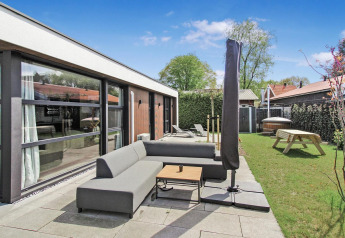Zona exterior en Eco Lodge de Uniq Leisure en Países Bajos, con sofá moderno, sombrilla y jardín verde.