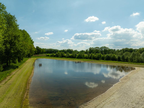 Lake with sandy beach at Holiday Resort 't Schuttenbelt, Overijssel, Netherlands, surrounded by trees.