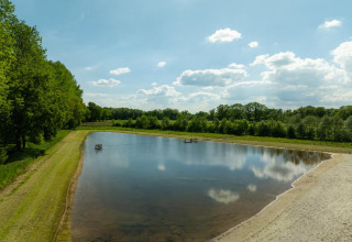 Lake with sandy beach at Holiday Resort 't Schuttenbelt, Overijssel, Netherlands, surrounded by trees.