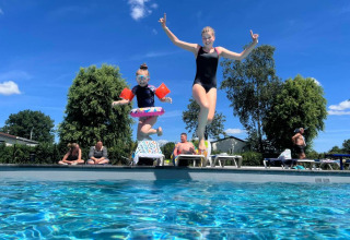 Two children jump into a pool at Vakantiepark de Zeeuwse Parel, Zeeland, Netherlands, on a sunny day.