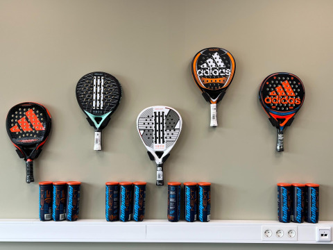 Palas y botes de pelotas Adidas de pádel expuestos en una pared en un parque vacacional en Zeeland, Países Bajos.