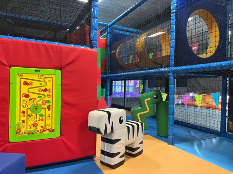 Zona de juegos interior para niños con estructuras blandas para escalar, toboganes y paneles de colores.