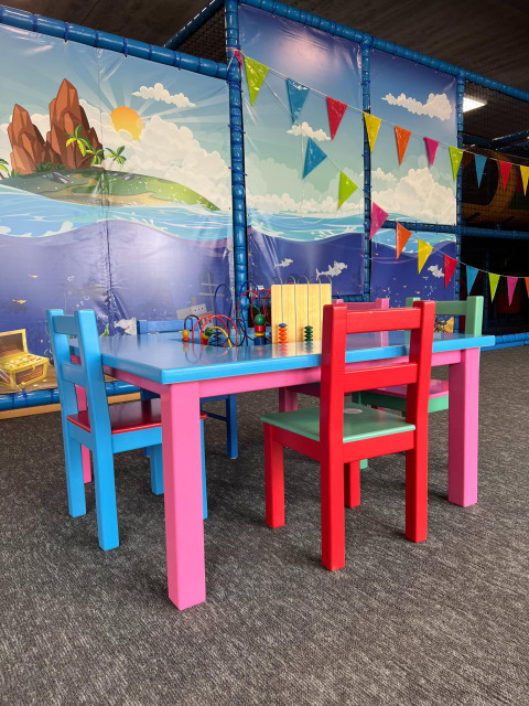 Colorida zona de juegos infantil con muebles brillantes, juguetes y mural marino en parque vacacional.