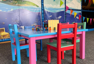 Colorida zona de juegos infantil con muebles brillantes, juguetes y mural marino en parque vacacional.