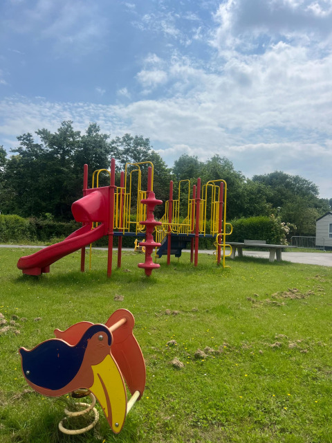 Parco giochi con scivolo e dondolo su prato sotto cielo azzurro al Vakantiepark de Zeeuwse Parel, Zeeland.