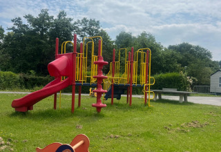 Spielplatz mit Rutsche und Wippe auf grünem Rasen unter blauem Himmel im Vakantiepark de Zeeuwse Parel.
