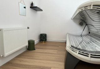 Stanza con lettino abbronzante, termosifone, piccolo specchio e mensola in un parco vacanze in Zeeland, Paesi Bassi.