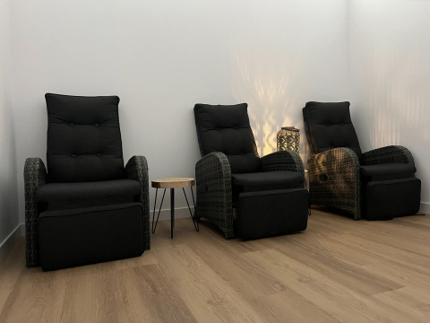 Trois fauteuils noirs avec repose-pieds et petite table dans une pièce au sol en bois et lumière tamisée.