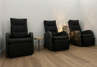 Three black lounge chairs with footrests and a small side table in a cozy room with wooden flooring.