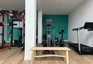 Salle de fitness au Vakantiepark de Zeeuwse Parel, Zélande avec équipements, banc de sport et tapis.