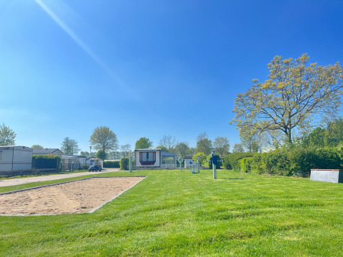 Ferienpark De Zeeuwse Parel in Zeeland mit Mobilheimen, Rasenflächen, Sandfläche und Bäumen bei blauem Himmel.