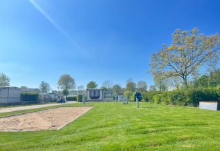 Parco vacanze De Zeeuwse Parel in Zelanda con case mobili, prato verde, campo di sabbia e alberi sotto cielo azzurro.