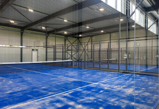 Indoor padel court with blue surface and black mesh walls at Vakantiepark de Zeeuwse Parel in Zeeland, Netherlands.