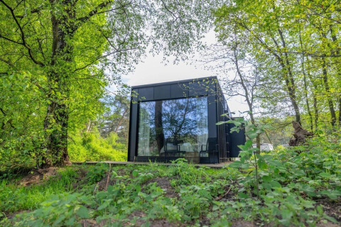 Nokken Forest Cabin, una tiny house negra con grandes ventanales en Wilsumer Berge, Alemania, entre árboles.
