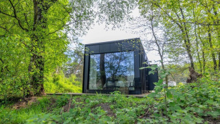 Nokken Forest Cabin, a black tiny house with large windows in Wilsumer Berge, Germany, surrounded by forest.