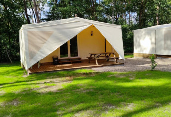 Glamping Coco Sweet lodge with a deck and picnic table, surrounded by greenery and trees in sunny weather.