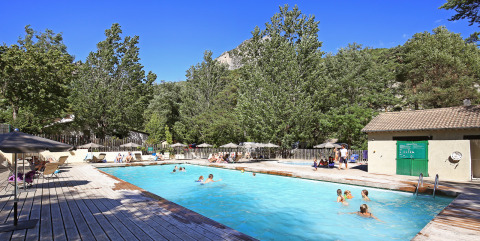 Piscina al aire libre rodeada de árboles en Huttopia Gorges du Verdon, un parque vacacional, en un día soleado.