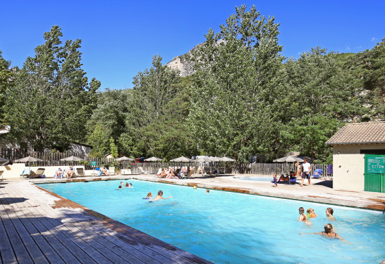 Udendørs swimmingpool omgivet af træer og ferieboliger ved Huttopia Gorges du Verdon på en solrig dag.