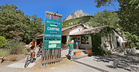 Cykler og gæster nyder sommeren ved Huttopia Gorges du Verdon campingplads, omgivet af bjerge og skov.