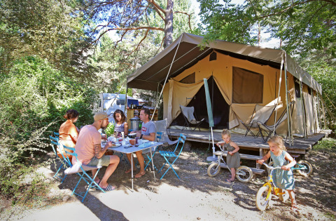 Familia desayunando al aire libre frente a una gran tienda de campaña en Huttopia Gorges du Verdon, Francia.