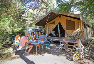 Familie nyder morgenmad udendørs foran et stort campingtelt i skoven ved Huttopia Gorges du Verdon.