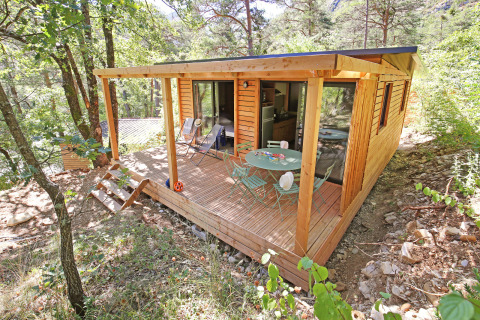 Cabina de glamping moderna de madera con terraza y muebles de exterior, en un parque de vacaciones boscoso.