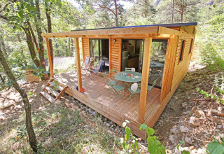 A modern wooden glamping cabin with a terrace and outdoor furniture in a peaceful forest holiday park.