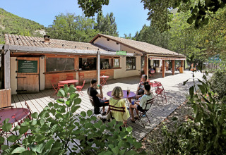 Udendørs caféområde på Huttopia Gorges du Verdon feriepark i Hauts-de-France, med gæster ved borde.