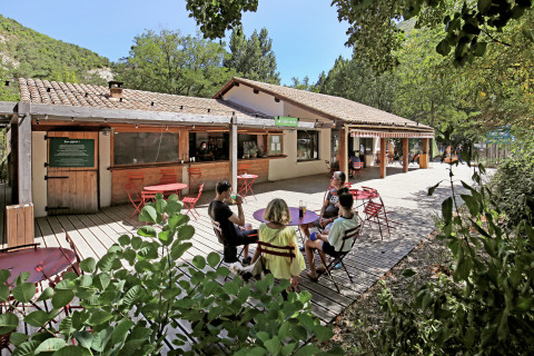 Area caffè all'aperto presso Huttopia Gorges du Verdon, Hauts-de-France, con ospiti seduti ai tavoli.