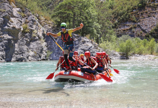 Gruppe iført redningsveste og hjelme nyder rafting i klart vand ved Huttopia Gorges du Verdon, Frankrig.