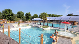 Zona de piscina al aire libre con niños, juegos acuáticos y piscina cubierta en Huttopia Baie du Mont St Michel.