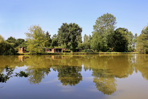 Wooden cabins by a lake with tree and sky reflections in the water at Huttopia Baie du Mont St Michel, Brittany, France.