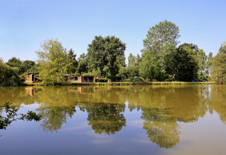 Casette di legno vicino a un lago con riflessi di alberi e cielo nell’acqua a Huttopia Baie du Mont St Michel, Bretagna, Francia.
