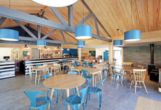 Moderne café med træloft, blå lamper og mix af stole ved Huttopia Baie du Mont St Michel, Bretagne, Frankrig.