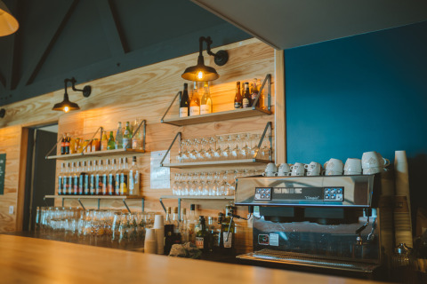 Bar en Huttopia Baie du Mont St Michel, Bretaña, Francia, con cafetera, vasos y botellas en las estanterías.