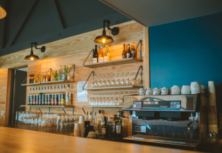 Bar im Huttopia Baie du Mont St Michel, Bretagne, mit Kaffeemaschine, Flaschen und Gläsern an den Regalen.
