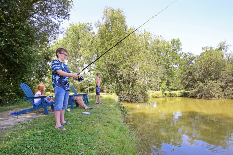 Niños y adultos pescando y relajándose junto a un lago en Huttopia Baie du Mont St Michel en Bretaña, Francia.