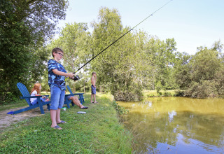 Niños y adultos pescando y relajándose junto a un lago en Huttopia Baie du Mont St Michel en Bretaña, Francia.