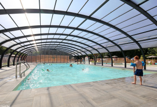 Indoor pool with glass roof, children swimming and a boy preparing to enter the water at Huttopia Baie du Mont St Michel.