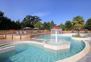 Outdoor swimming pool with water fountain, sun loungers and umbrellas at Huttopia Baie du Mont St Michel, Brittany