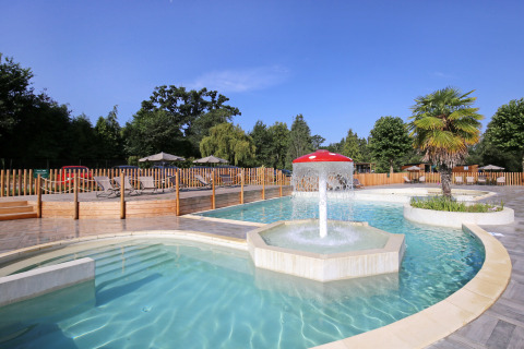 Outdoor swimming pool with water fountain, sun loungers and umbrellas at Huttopia Baie du Mont St Michel, Brittany