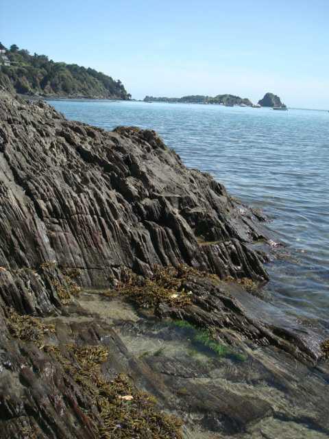 Costa rocosa en Huttopia Baie du Mont St Michel, Bretaña, Francia, junto a aguas tranquilas y claras.
