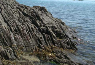 Costa rocosa en Huttopia Baie du Mont St Michel, Bretaña, Francia, junto a aguas tranquilas y claras.