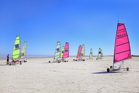 Carros a vela en la playa en Huttopia Baie du Mont St Michel, parque de vacaciones en Bretaña, Francia, bajo cielo azul.