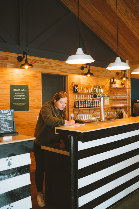 Woman writing behind black-and-white bar in wooden interior at Huttopia Baie du Mont St Michel, Brittany, France.