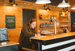 Vrouw schrijft achter gestreepte bar bij Huttopia Baie du Mont St Michel, Bretagne, Frankrijk, vakantiestemming.
