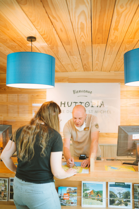 Rezeptionist hilft einer Frau in der Lobby von Huttopia Baie du Mont St Michel, Bretagne, Frankreich.
