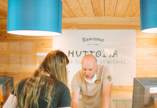 Rezeptionist hilft einer Frau in der Lobby von Huttopia Baie du Mont St Michel, Bretagne, Frankreich.